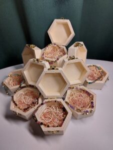 Zestaw małych sześciokątnych drewnianych pudełek, z których każde zawiera kolorową bransoletkę i ozdobne wypełnienie.